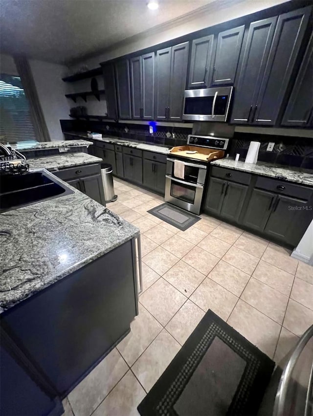1030 Marcello Blvd, Kissimmee, FL 34746 - kitchen with light tile patterned floors, dark cabinets, a sink, stainless steel appliances, and light stone counters