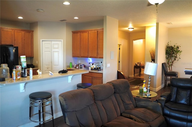 kitchen with brown cabinetry, a breakfast bar, freestanding refrigerator, open floor plan, and light countertops