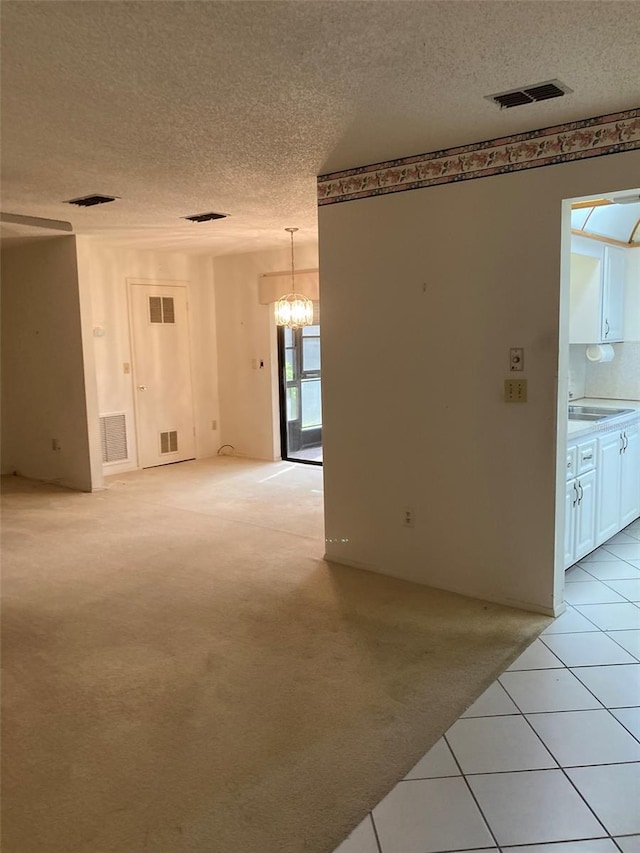 unfurnished room featuring light colored carpet, a textured ceiling, a chandelier, and visible vents