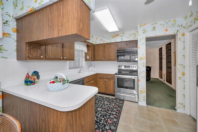 kitchen featuring black appliances, a peninsula, wallpapered walls, light countertops, and a sink
