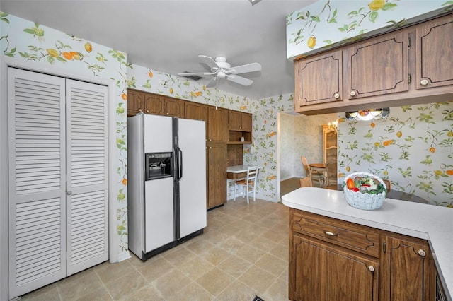 kitchen featuring white refrigerator with ice dispenser, wallpapered walls, ceiling fan, light countertops, and brown cabinets
