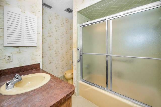 bathroom featuring wallpapered walls, shower / bath combination with glass door, toilet, vanity, and a textured ceiling