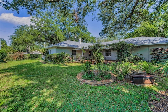 rear view of property with stucco siding, a lawn, and a chimney
