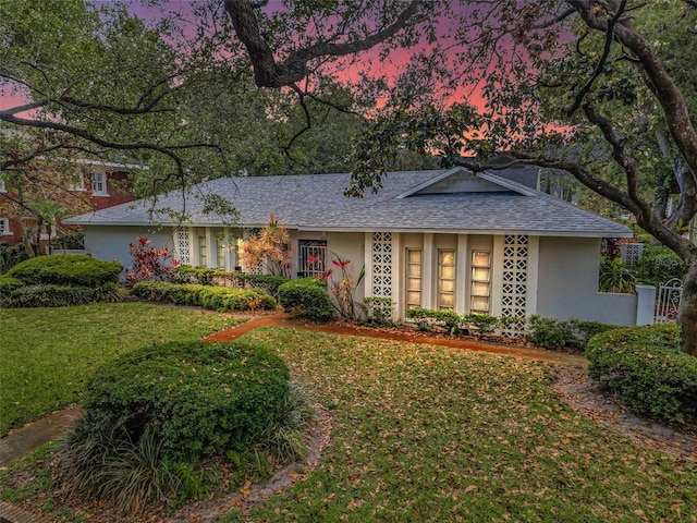 view of front of home with a lawn, stucco siding, and roof with shingles