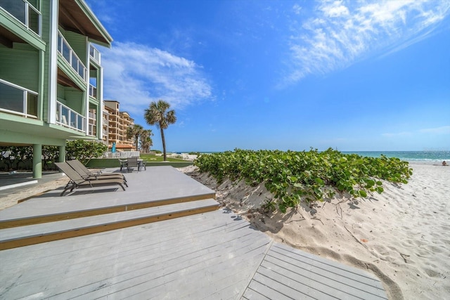 view of patio with a deck with water view, a beach view, and outdoor dining space