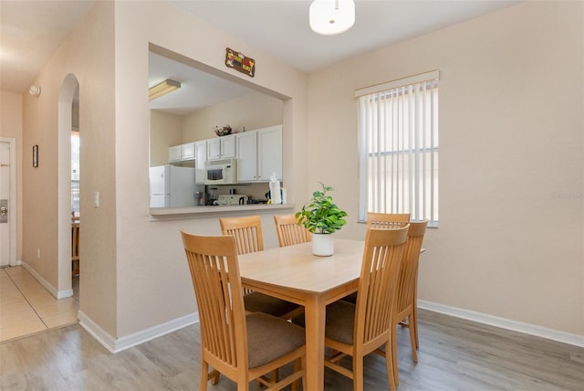 dining room featuring arched walkways, light wood finished floors, and baseboards