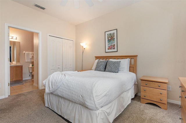 carpeted bedroom with a closet, baseboards, tile patterned flooring, ensuite bathroom, and a ceiling fan