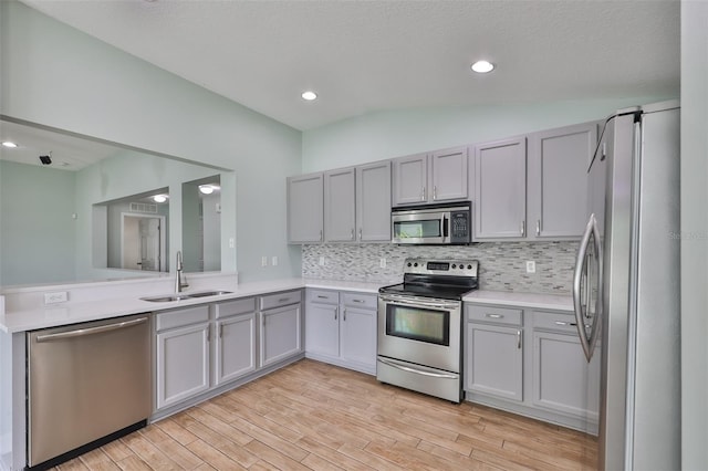 kitchen featuring a sink, stainless steel appliances, gray cabinets, decorative backsplash, and light wood-style floors