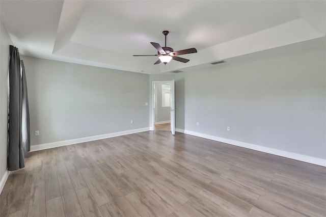 unfurnished room with wood finished floors, a tray ceiling, visible vents, baseboards, and ceiling fan