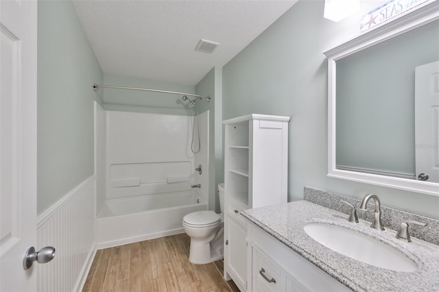 bathroom with toilet, a wainscoted wall, wood finished floors, vanity, and bathing tub / shower combination