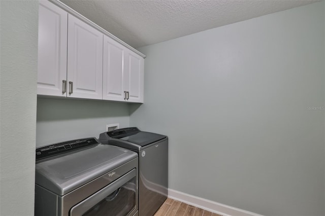 laundry room featuring washing machine and dryer, light wood-style flooring, cabinet space, a textured ceiling, and baseboards