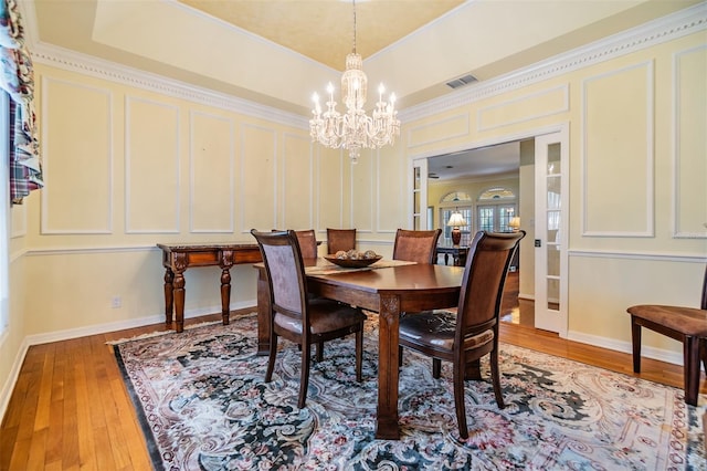 2769 St Andrews Blvd, Tarpon Springs, FL 34688 - dining space with a decorative wall, a chandelier, light wood finished floors, ornamental molding, and a raised ceiling