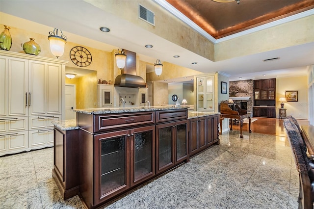2769 St Andrews Blvd, Tarpon Springs, FL 34688 - kitchen with open floor plan, wall chimney exhaust hood, glass insert cabinets, light stone countertops, and a large fireplace