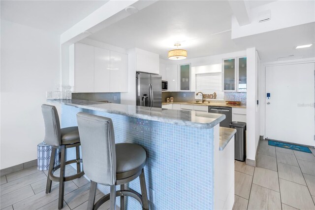kitchen featuring appliances with stainless steel finishes, a peninsula, a kitchen breakfast bar, a sink, and white cabinets
