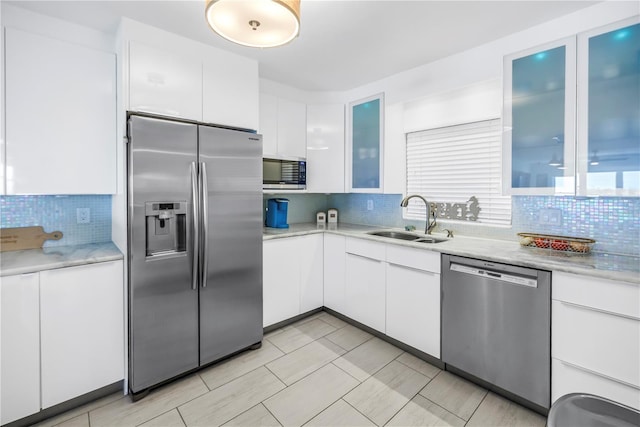 kitchen with stainless steel appliances, a sink, decorative backsplash, white cabinets, and glass insert cabinets