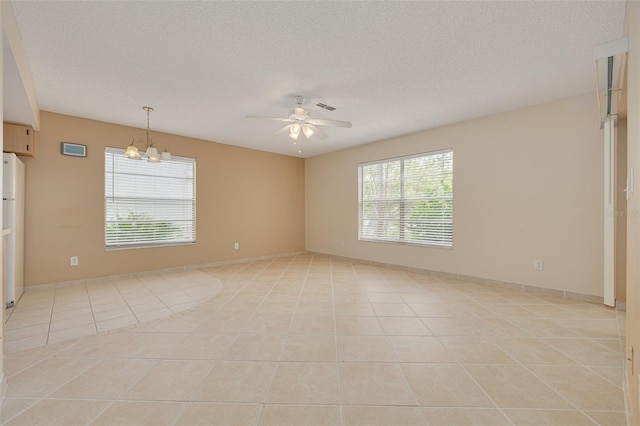 unfurnished room featuring light tile patterned floors, a ceiling fan, plenty of natural light, a textured ceiling, and a chandelier