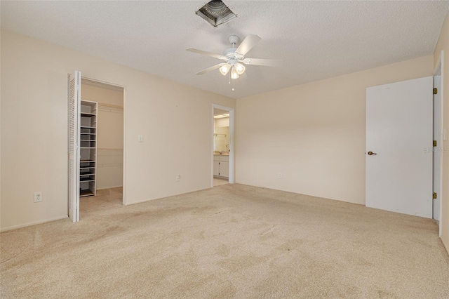 unfurnished bedroom with carpet, a spacious closet, ensuite bath, ceiling fan, and a closet