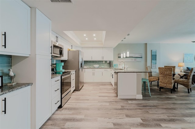 400 Island Way Unit 1709, Clearwater Beach, FL 33767 - kitchen with stainless steel appliances, light wood-style floors, a tray ceiling, a peninsula, and dark stone countertops