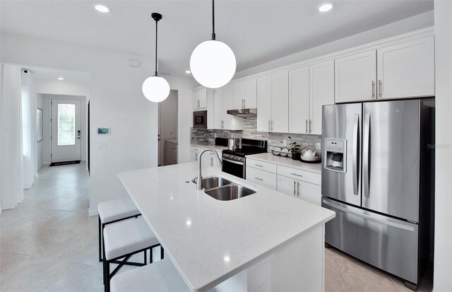 kitchen with appliances with stainless steel finishes, a sink, under cabinet range hood, white cabinetry, and an island with sink