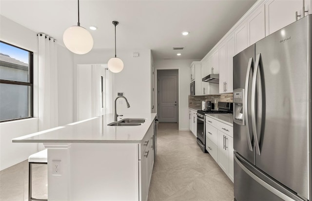 kitchen with stainless steel appliances, a sink, under cabinet range hood, tasteful backsplash, and a center island with sink