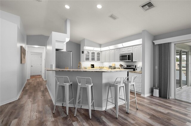5193 Boyle Ter, Port Charlotte, FL 33981 - kitchen with appliances with stainless steel finishes, a kitchen breakfast bar, glass insert cabinets, wood finished floors, and light stone counters