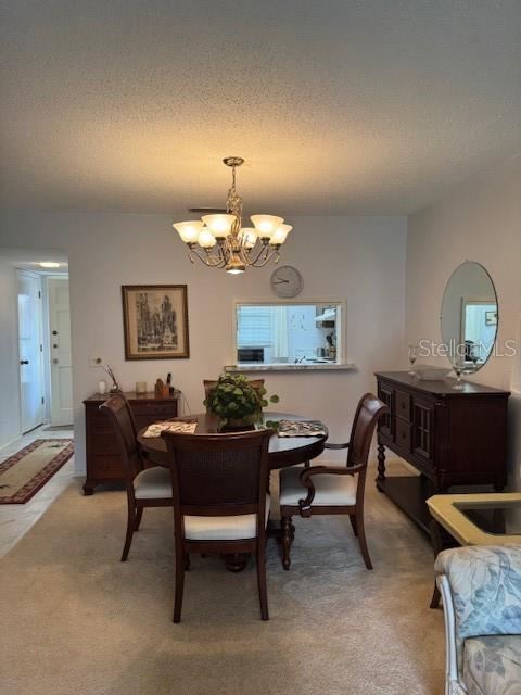 dining area with an inviting chandelier, a textured ceiling, and light colored carpet