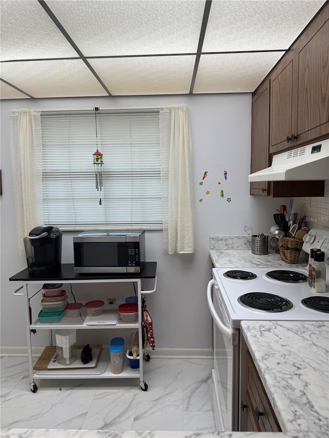 kitchen with stainless steel microwave, electric range, marble finish floor, under cabinet range hood, and a drop ceiling