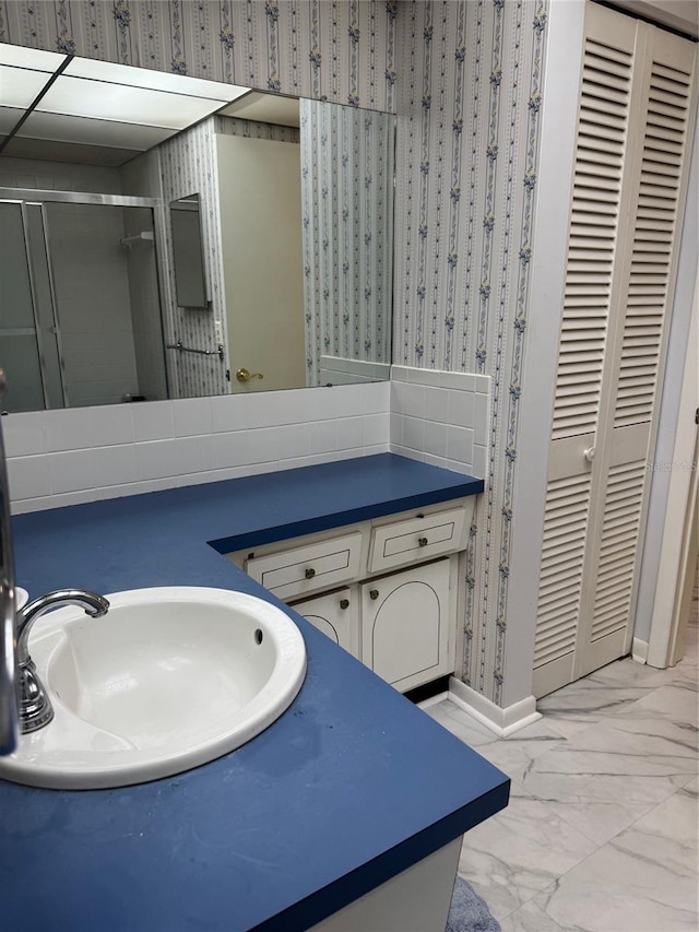 bathroom featuring marble finish flooring, a stall shower, vanity, wallpapered walls, and baseboards