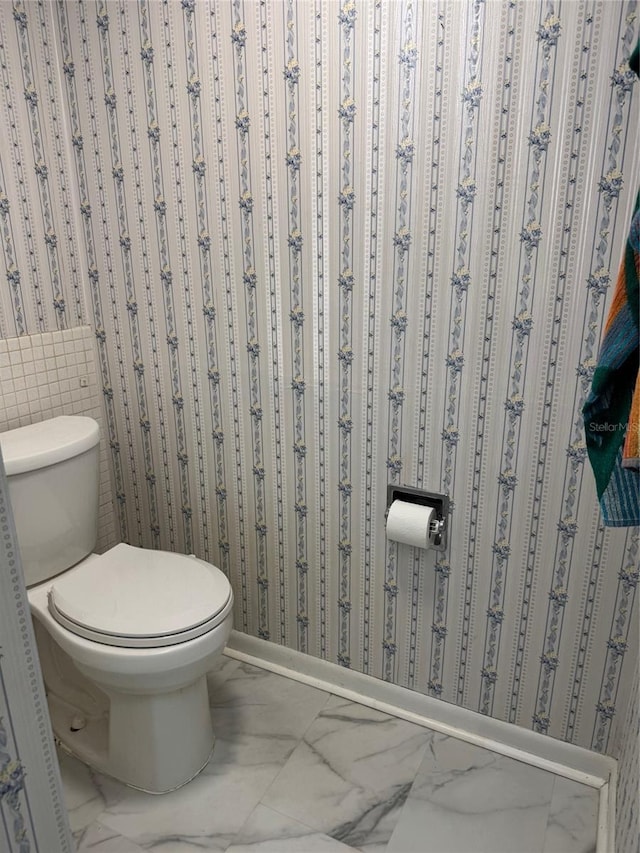 bathroom with marble finish floors, toilet, wallpapered walls, and baseboards
