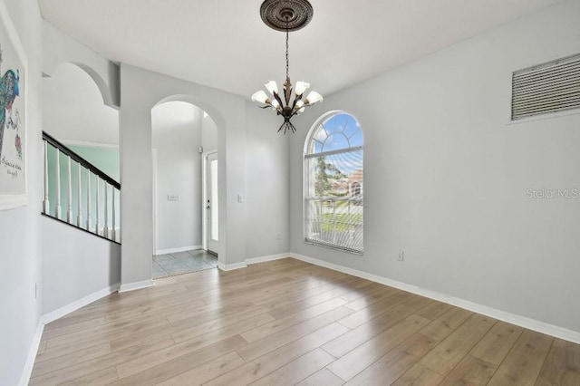 27012 Sea Breeze Way, Wesley Chapel, FL 33544 - spare room featuring a chandelier, light wood-style floors, arched walkways, and baseboards