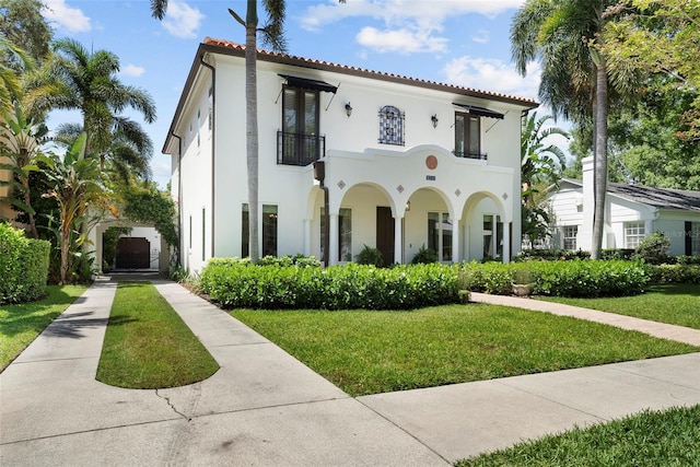 mediterranean / spanish-style home featuring a balcony, concrete driveway, a front lawn, and stucco siding