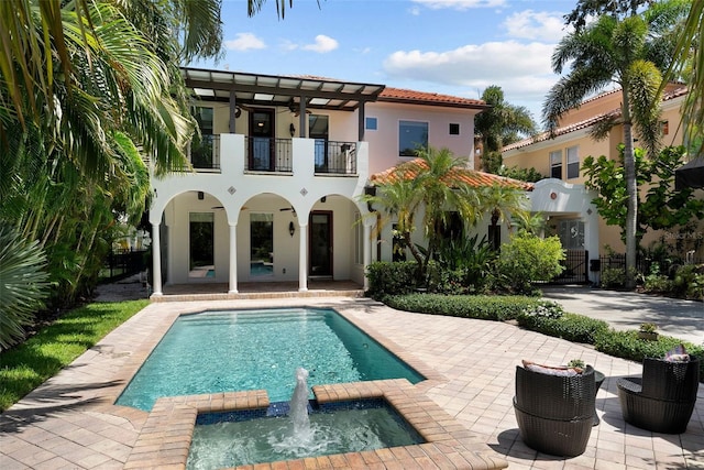 rear view of house with a balcony, a patio area, stucco siding, a pool with connected hot tub, and fence