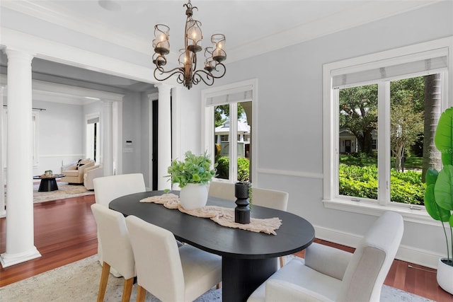 dining room featuring wood finished floors, a chandelier, ornate columns, ornamental molding, and baseboards