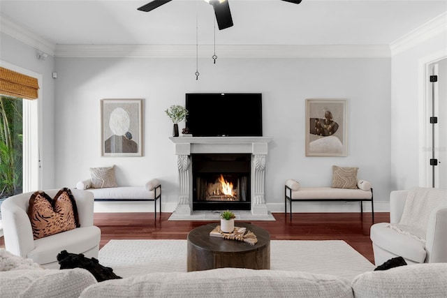 living room with wood finished floors, ornamental molding, a ceiling fan, a lit fireplace, and baseboards