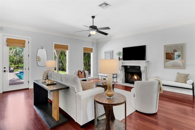 living area with dark wood-type flooring, crown molding, ceiling fan, and a premium fireplace