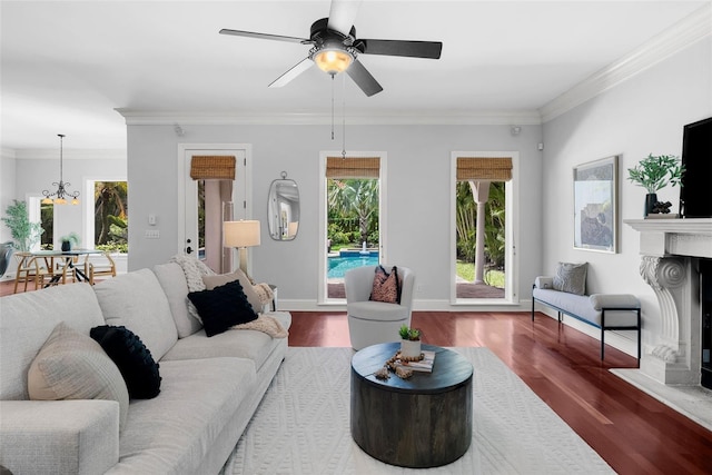 living room featuring wood finished floors, a chandelier, a fireplace, ornamental molding, and a ceiling fan