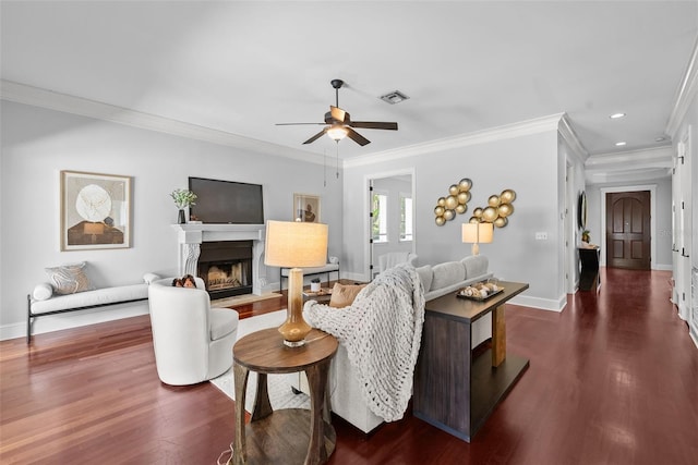 living room with dark wood-style flooring, ceiling fan, baseboards, ornamental molding, and a premium fireplace