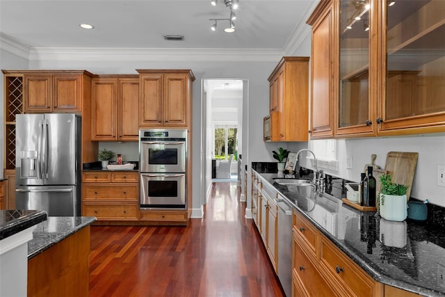kitchen featuring stainless steel appliances, a sink, brown cabinets, dark wood-style flooring, and crown molding
