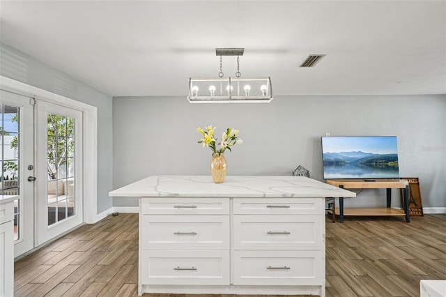 6010 Bayou Grande Blvd NE, Saint Petersburg, FL 33703 - kitchen with wood finished floors, white cabinetry, light stone countertops, french doors, and decorative light fixtures