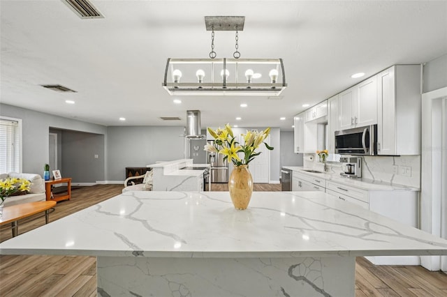 6010 Bayou Grande Blvd NE, Saint Petersburg, FL 33703 - kitchen featuring stainless steel appliances, a kitchen island, wood finished floors, white cabinetry, and light stone counters