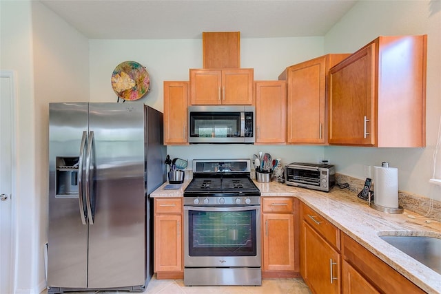 kitchen with stainless steel appliances, light stone countertops, light tile patterned flooring, and a sink