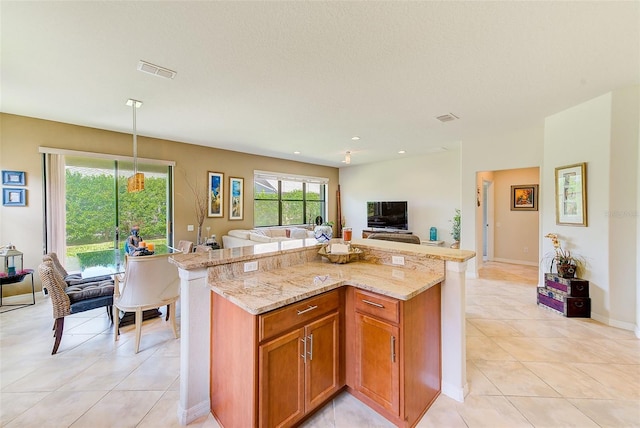 kitchen with open floor plan, light tile patterned flooring, light stone countertops, brown cabinets, and a center island