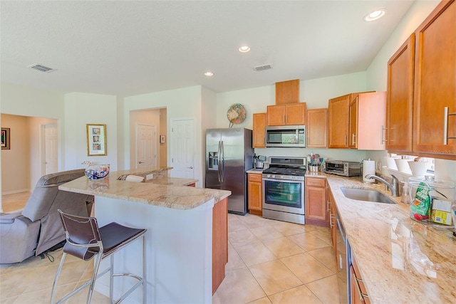 kitchen with appliances with stainless steel finishes, a sink, a kitchen bar, light stone counters, and a center island