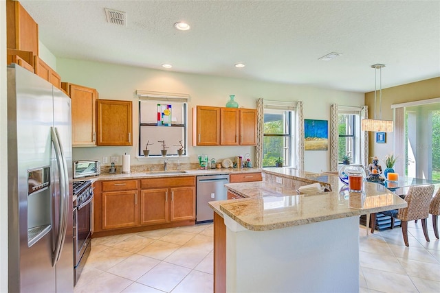 kitchen with stainless steel appliances, a sink, brown cabinetry, recessed lighting, and a textured ceiling
