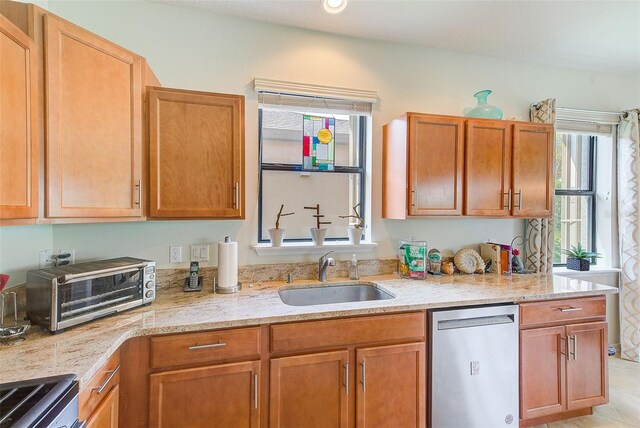 kitchen with stainless steel appliances, a sink, light stone counters, and brown cabinets