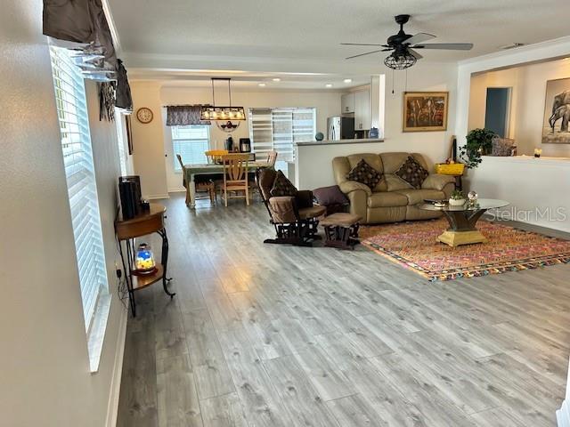 living area with ceiling fan, wood finished floors, and crown molding