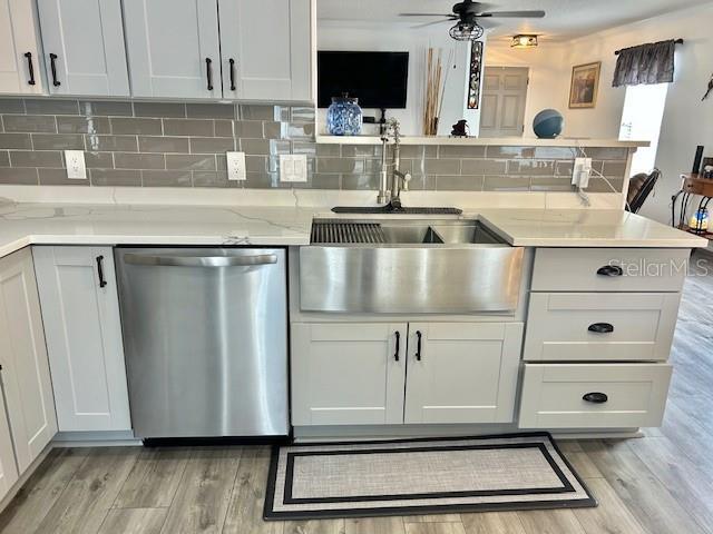 kitchen with dishwasher, light wood finished floors, a ceiling fan, a sink, and a peninsula