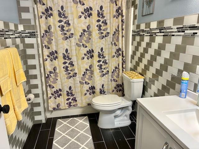 bathroom with tile walls, toilet, vanity, shower / tub combo with curtain, and tile patterned flooring