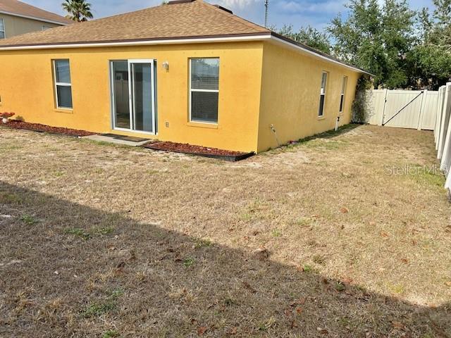 back of house featuring stucco siding, a gate, and roof with shingles