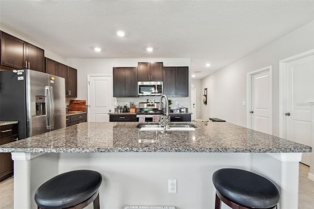 kitchen with stainless steel appliances, dark brown cabinets, a breakfast bar, and a sink